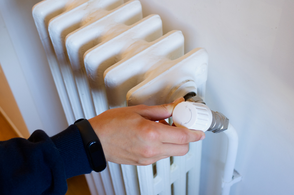 A hand rests on the control knob of a radiatior, the plus and minus signs are visible.