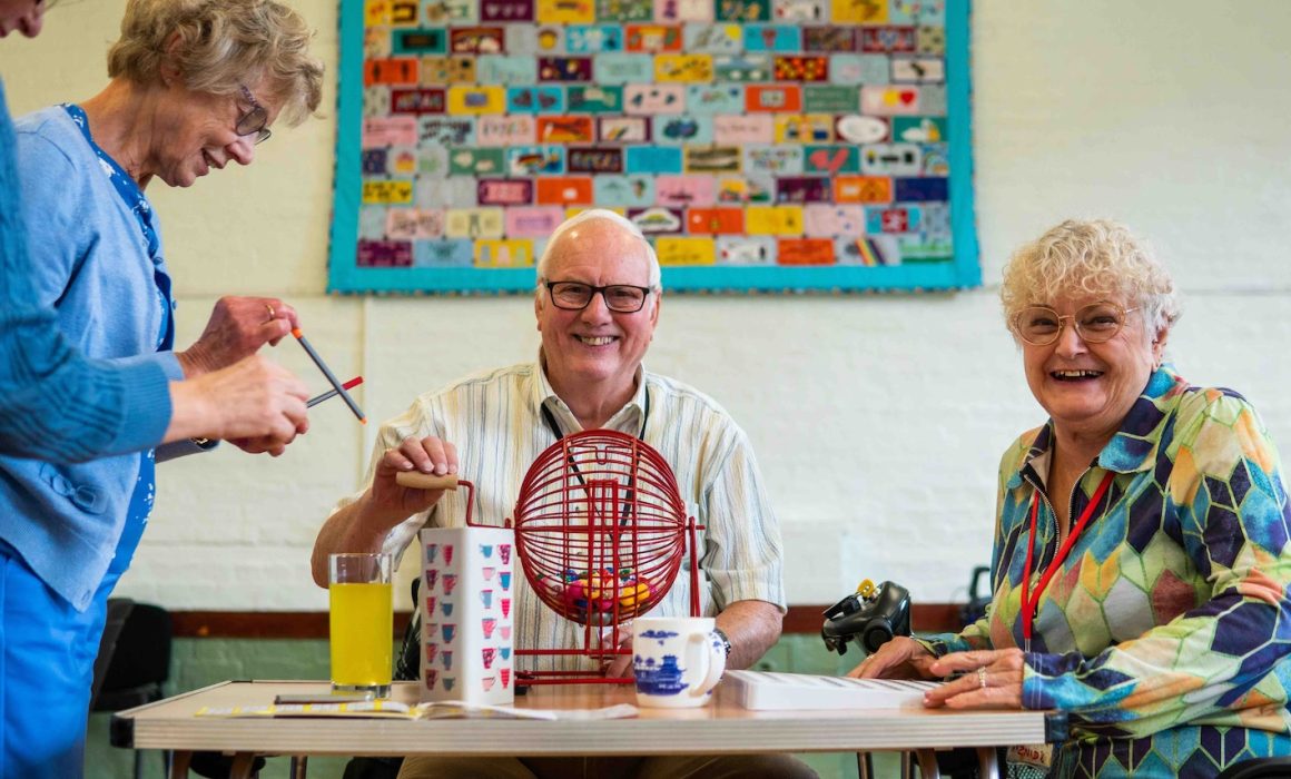 Two older women and a men at a table in a community space, they are playing games and smiling