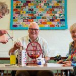 Two older women and a men at a table in a community space, they are playing games and smiling